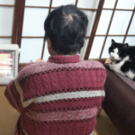 小さい電気ストーブの前に座る母と猫の画像