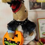 いつもの服に追加で、マントと帽子を付けて、カボチャの形のバッグを下げているうさぎのぬいぐるみの画像