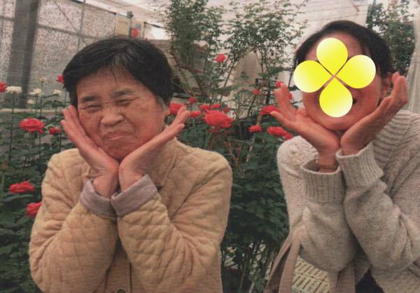 バラの花の前で、手を花の形にしたポーズをとるわたしと母の画像