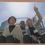 雲のない空の下、展望台で上を指さす職員と母の画像