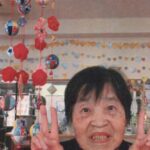 ひな祭りの吊るし飾りの前でダブルピースをする母の画像