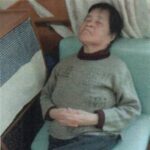 椅子にふんぞり返って座り、足を組んで寝ている母の画像