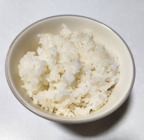 白いテーブルの上、内側が白色のお茶碗に盛られた白ご飯の画像